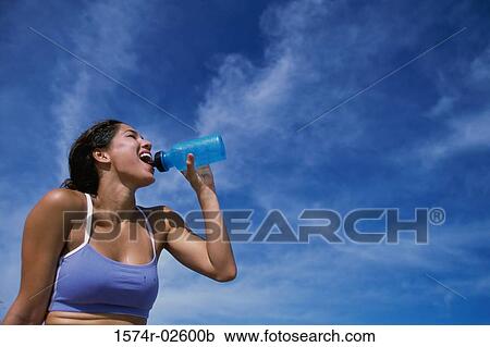 Low angle view of a young woman drinking water from a bottle View Large Photo Image Stock Image - Low angle view of a young woman drinking water from a bottle. Fotosearch