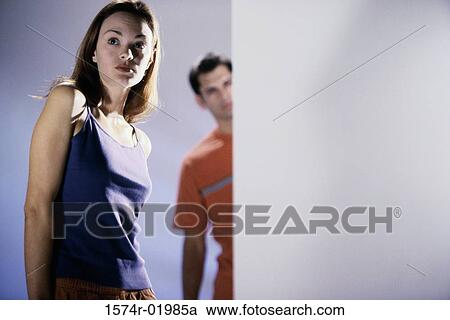 Stock Image - Low angle view of a young woman with a young man standing behind her. Fotosearch