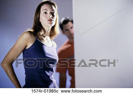 Stock Image - Low angle view of a young woman with a young man standing behind her. Fotosearch