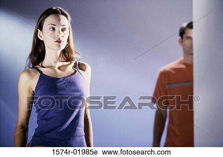 Stock Image - Low angle view of a young woman with a young man standing behind her. Fotosearch