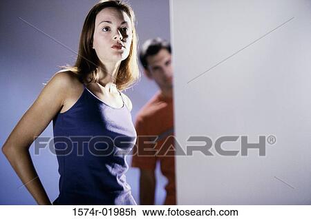Stock Image - Low angle view of a young woman with a young man standing behind her. Fotosearch