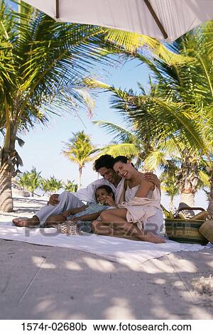 Stock Image - Low angle view of parents sitting with their daughter on the beach. Fotosearch