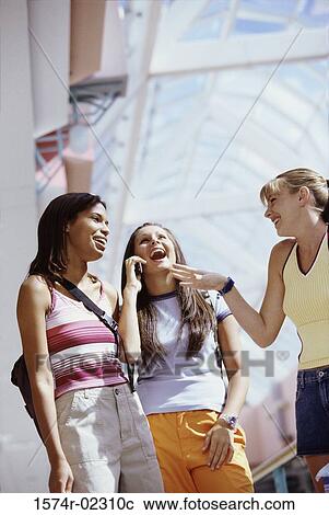 Stock Image - Low angle view of three teenage girls standing in a shopping mall. Fotosearch