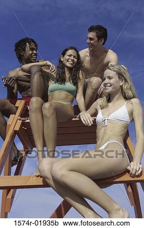 Stock Image - Low angle view of two teenage couples sitting on a lifeguard chair. Fotosearch