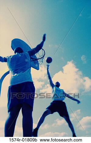 Stock Image - Low angle view of two young men playing basketball. Fotosearch