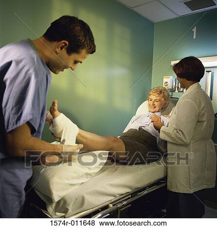 Stock Photo - Male doctor dressing a senior woman's foot with a female doctor holding her hand. Fotosearch