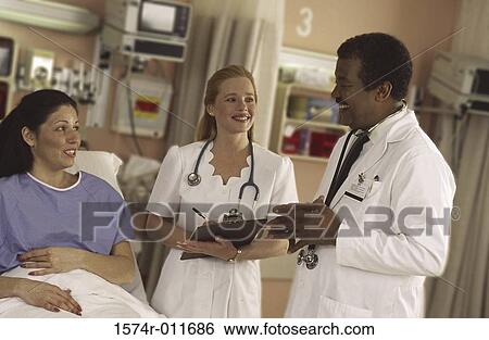 Stock Photograph - Male doctor standing with a female nurse talking to a female patient. Fotosearch