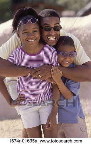 Stock Image - Man hugging his son and daughter on the beach. Fotosearch