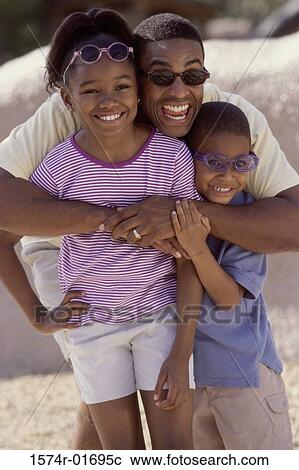 Stock Image - Man hugging his son and daughter on the beach. Fotosearch