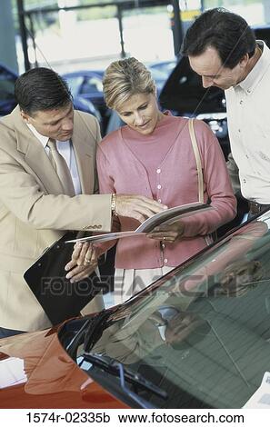 Mid adult couple looking at a brochure in a car showroom View Large Photo Image Stock Image - Mid adult couple looking at a brochure in a car showroom. Fotosearch