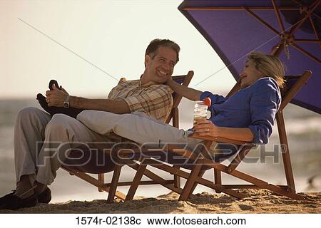 Mid adult couple sitting on lounge chairs on the beach View Large Photo Image Stock Image - Mid adult couple sitting on lounge chairs on the beach. Fotosearch
