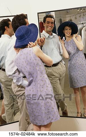 Stock Image - Mid adult couple standing in front of a mirror in the fitting room of a clothing store. Fotosearch