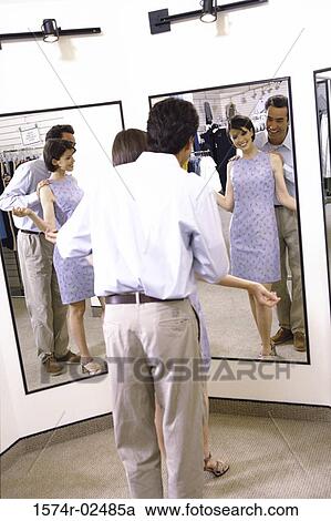 Stock Image - Mid adult couple standing in front of a mirror in the fitting room of a clothing store. Fotosearch