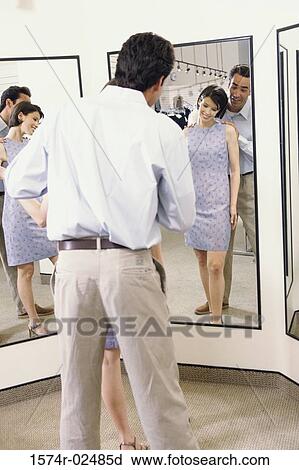 Mid adult couple standing in front of a mirror in the fitting room of a clothing store View Large Photo Image Stock Image - Mid adult couple standing in front of a mirror in the fitting room of a clothing store. Fotosearch