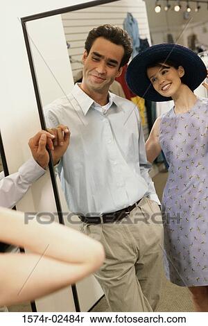 Stock Photography - Mid adult couple standing in front of a mirror in the fitting room of a clothing store. Fotosearch