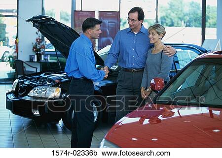Stock Image - Mid adult couple talking to a car salesman in a car showroom. Fotosearch