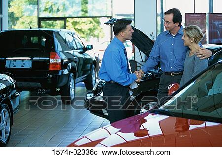 Stock Image - Mid adult couple talking to a car salesman in a car showroom. Fotosearch