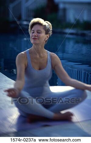 Stock Image - Mid adult woman sitting on the floor meditating. Fotosearch