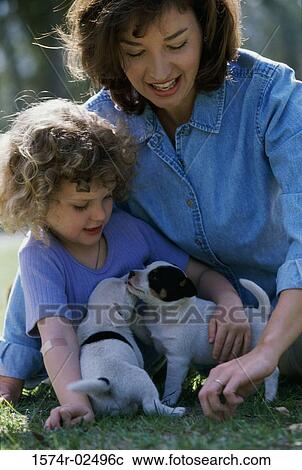 Stock Image - Mother and her daughter playing with puppies. Fotosearch