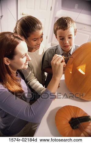 Stock Image - Mother carving a pumpkin with her son and daughter. Fotosearch