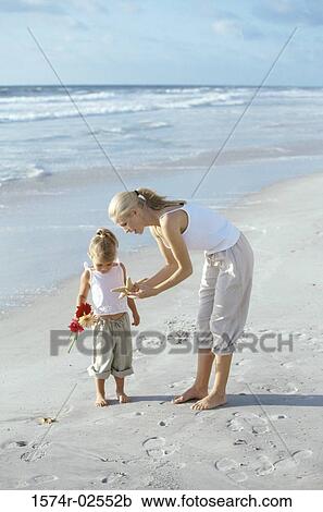Stock Image - Mother showing her daughter a starfish on the beach. Fotosearch
