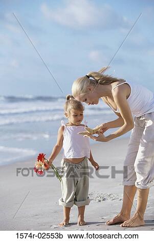 Stock Image - Mother showing her daughter a starfish on the beach. Fotosearch
