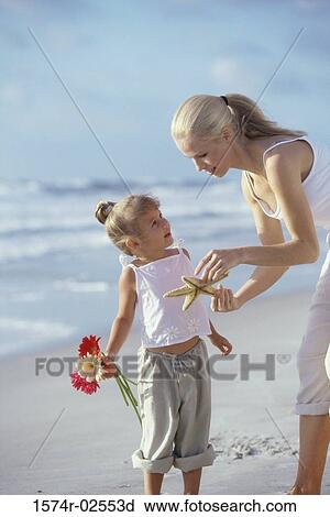 Stock Image - Mother showing her daughter a starfish on the beach. Fotosearch