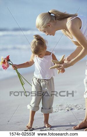 Stock Image - Mother showing her daughter a starfish on the beach. Fotosearch