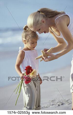 Stock Image - Mother showing her daughter a starfish on the beach. Fotosearch