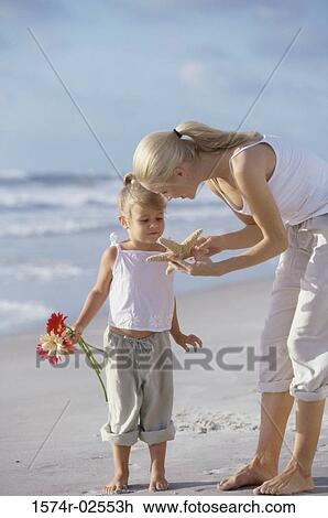 Stock Image - Mother showing her daughter a starfish on the beach. Fotosearch