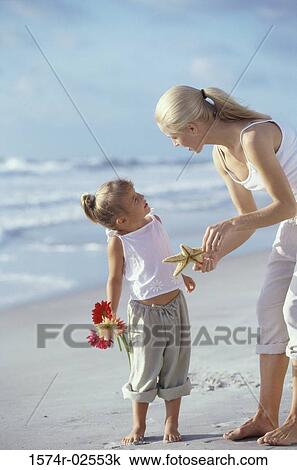 Stock Image - Mother showing her daughter a starfish on the beach. Fotosearch