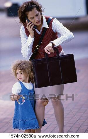 Mother talking on a mobile phone with her daughter standing beside her View Large Photo Image Stock Image - Mother talking on a mobile phone with her daughter standing beside her. Fotosearch