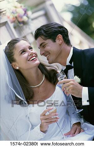 Newlywed couple smiling while holding glasses of champagne View Large Photo Image Stock Photograph - Newlywed couple smiling while holding glasses of champagne. Fotosearch