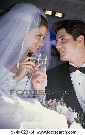 Stock Image - Newlywed couple toasting with champagne glasses in a car. Fotosearch