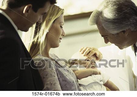 Stock Image - Parents and their baby girl during a baptism ceremony. Fotosearch