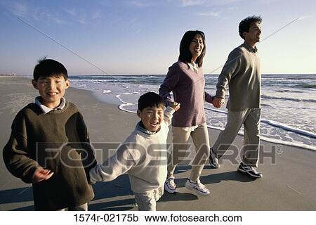 Stock Image - Parents and their two sons holding hands walking on the beach. Fotosearch