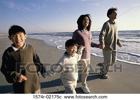 Stock Image - Parents and their two sons holding hands walking on the beach. Fotosearch