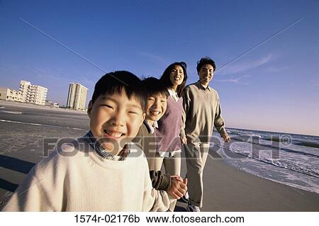 Stock Image - Parents and their two sons holding hands walking on the beach. Fotosearch