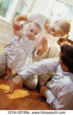 Stock Image - Parents helping their baby girl learn how to walk. Fotosearch