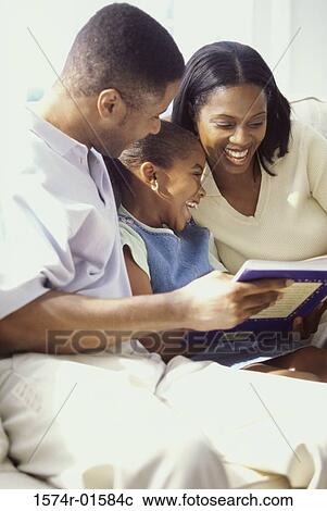 Stock Image - Parents reading a book with their daughter. Fotosearch