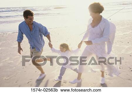 Stock Image - Parents running on the beach with their daughter. Fotosearch