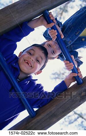 Stock Image - Portrait of a boy and a girl climbing on monkey bars. Fotosearch