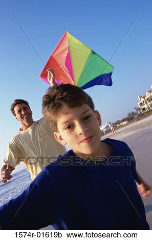 Stock Image - Portrait of a boy boy flying a kite with his father at the beach. Fotosearch