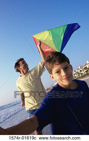 Stock Image - Portrait of a boy boy flying a kite with his father at the beach. Fotosearch