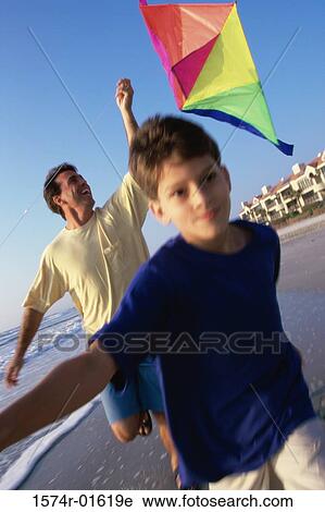 Stock Image - Portrait of a boy boy flying a kite with his father at the beach. Fotosearch