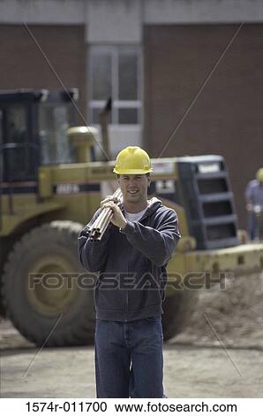 Stock Image - Portrait of a construction worker carrying metal pipes on his shoulder. Fotosearch