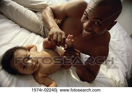Stock Image - Portrait of a father holding his baby boy's feet. Fotosearch