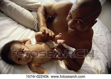 Stock Image - Portrait of a father holding his baby boy's feet. Fotosearch
