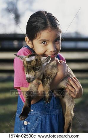Stock Image - Portrait of a girl holding a kid goat in her arms. Fotosearch