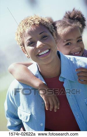 Stock Image - Portrait of a girl riding piggyback on her mother. Fotosearch